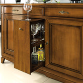 Dettaglio della credenza classica in legno di ciliegio con anta centrale portabottiglie aperta, dotata di ripiani interni per bottiglie e bicchieri. Il mobile presenta due ante laterali, eleganti maniglie in ottone e una finitura calda. Parte della collezione Arte d’Este Piombini.